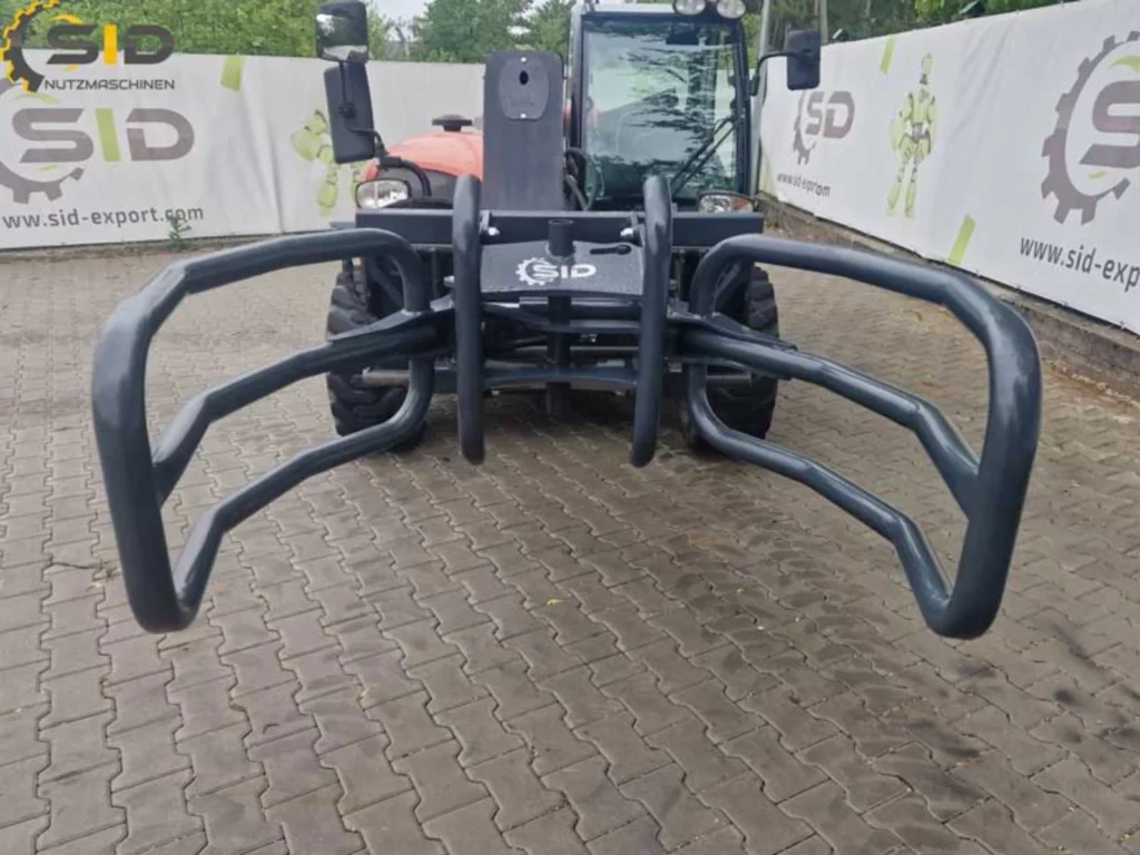 Hydraulische Ballenzange greift präzise einen Rundballen für den sicheren Transport auf einem landwirtschaftlichen Hof.